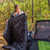an in use shot of a person utilizing their black shell lightweight down blanket style sleeping bag quilt with a navy blue interior in nature
