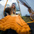 in use shot of orange lightweight, comfortable, cost effective, packable,  sleeping pad made from light fabrics and polyester being used as a bed in a tent campsite