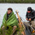 a picture of two menone wrapped in a forest green revelation synthetic sleeping quilt and the other in a black torrid jacket by a lake staying warm