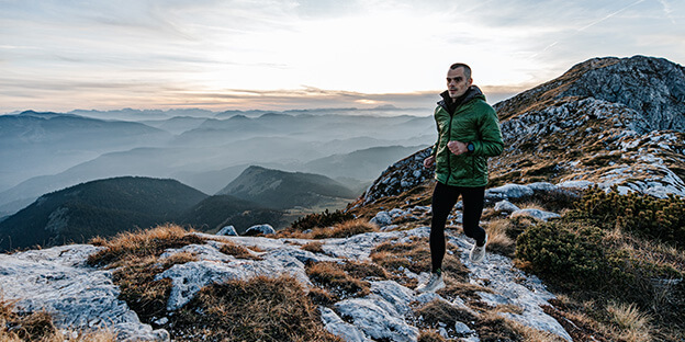 A picture of a man running in the mountains with a forest color torrid jacket on