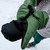 in use shot of fern green all weather performance, washable, packable, lightweight, mittens with a black liner being used to keep there hands warm in cold weather